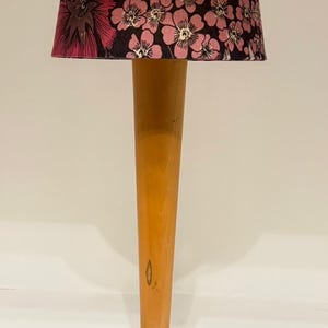 May include: A table lamp with a floral lampshade. The lampshade has pink flowers on a black background. The lamp has a wooden stem and a chrome base. The lamp is designed for indoor use.