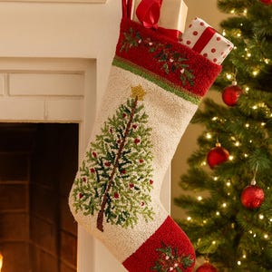 May include: A Christmas stocking with a festive design. The stocking is primarily off-white with a green Christmas tree and red berries. The top and toe are red, and it's filled with wrapped gifts. It hangs from a white mantel.