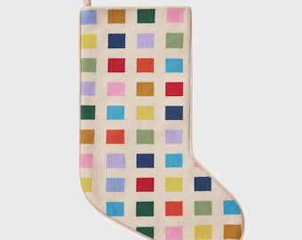 May include: A Christmas stocking with a cream-colored background and a pattern of colorful squares. The squares are in shades of red, blue, green, yellow, orange, pink, and purple. The stocking has a loop for hanging.
