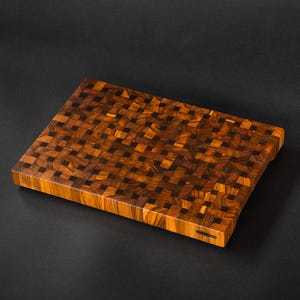 Puede incluir: Tabla de cortar rectangular de madera con un diseño único de bloque de carnicero de testa. La tabla presenta un patrón de mosaico de piezas de madera marrón oscuro y claro. Mide aproximadamente 46 cm de largo y 30 cm de ancho.