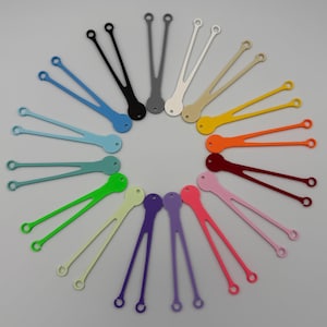 May include: A selection of brightly coloured silicone cable ties, arranged in a circular pattern. The ties are in shades of blue, black, grey, white, beige, yellow, orange, red, pink, purple, and green. Each tie has a loop at each end.