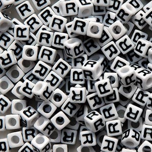 May include: A close-up image of a pile of white plastic letter beads with the letter "R" printed in black on each bead.