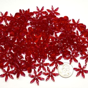 May include: A large quantity of red plastic flower-shaped embellishments. The embellishments are scattered on a white surface. A US quarter is included for scale.