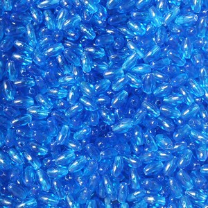 May include: A large quantity of small, translucent blue oval-shaped beads. The beads are made of glass or plastic and have a smooth, shiny finish.