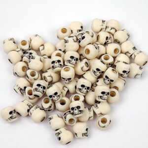 May include: A large pile of white skull-shaped beads with black painted details. The beads have a hole through the center for stringing.