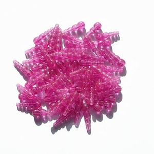 May include: A pile of translucent, hot pink plastic beads. Each bead is composed of a series of small, rounded segments, connected to form a long, slender shape. The beads are scattered on a white surface, casting shadows.