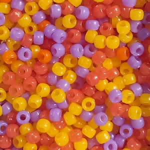 May include: A close-up image of a large pile of colorful plastic beads. The beads are in shades of yellow, orange, and purple.