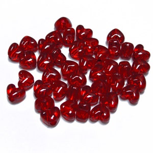 May include: A large pile of red heart-shaped beads. The beads are made of glass and have a shiny finish.