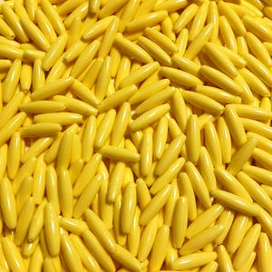 May include: A close-up shot of a pile of yellow, oblong beads. The beads are smooth and evenly colored, with a slight sheen. They are scattered randomly, filling the frame. The overall impression is of a bright, cheerful collection of craft supplies.