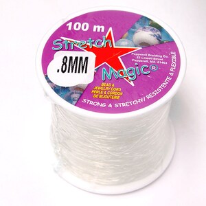 May include: A spool of clear, stretchy beading cord, labeled "Stretch Magic." The label is purple with a red star and white text indicating the cord is 0.8mm thick and 100 meters long. The packaging also states the cord is strong and flexible.