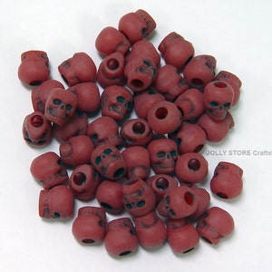 May include: A pile of red plastic skull beads. The beads have a hole in the top for stringing.