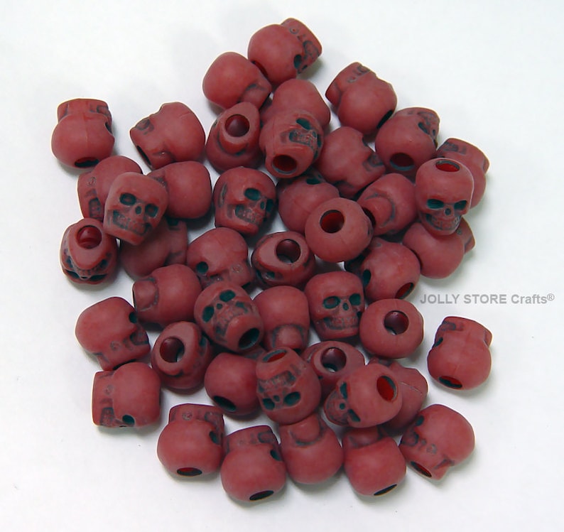 May include: A pile of red plastic skull beads. The beads have a hole in the top for stringing.