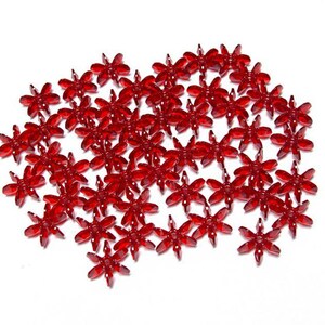 May include: A large group of red, star-shaped, plastic embellishments. The embellishments are scattered on a white surface.