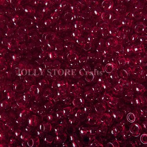 May include: A close-up image of a large quantity of small, round, transparent red beads. The beads are all the same size and shape, and they are arranged in a random pattern.