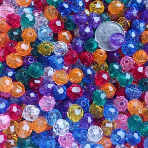 May include: A vibrant assortment of faceted beads in various colors, including red, orange, green, blue, and purple. A US dime is included for size reference. These beads are ideal for jewelry making and crafting projects.