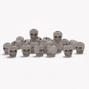 May include: A group of 18 small, white, plastic skull beads. The beads are all the same size and shape, and they are arranged in a random pattern.