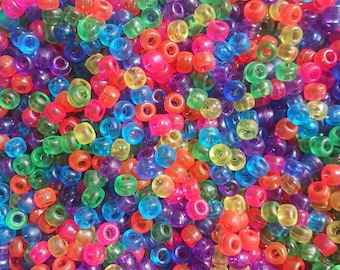 Puede incluir: Primer plano de una colección de cuentas de plástico de colores brillantes. Las cuentas son de color rojo, naranja, amarillo, verde, azul y morado. Cada cuenta cilíndrica y translúcida tiene un agujero en el centro, ideal para manualidades.