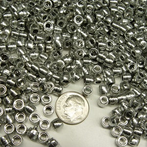 May include: A large quantity of silver-colored lead shot, used for reloading ammunition, is displayed on a white surface. A US dime coin is included for scale.