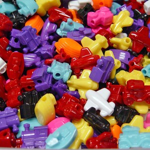 May include: A large collection of colorful plastic toy beads in the shapes of airplanes, cars, trains, and other vehicles. The beads are perfect for crafting and making jewelry.