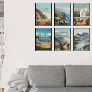 Peut inclure: Un ensemble de six affiches de voyage encadr&eacute;es illustrant Uluru Kata Tjuta, La Palma, le parc national de Yellowstone, le Kirghizistan, les Highlands &eacute;cossais avec une vache Highland et la Tasmanie, dispos&eacute;es sur deux rang&eacute;es sur un mur blanc.
