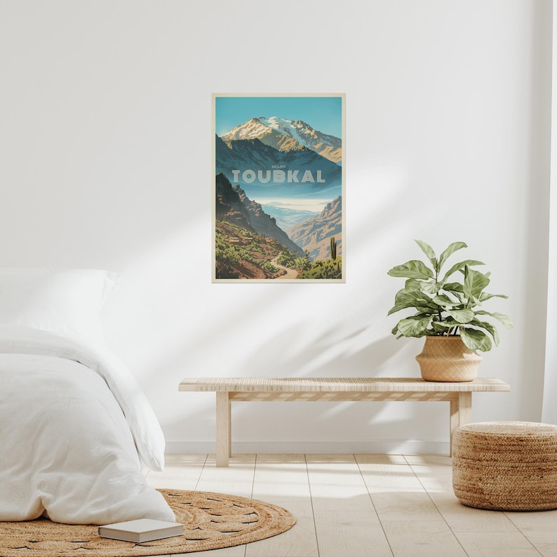 Peut inclure: Une affiche murale rectangulaire pr&eacute;sentant une illustration paysag&egrave;re stylis&eacute;e du mont Toubkal. L'&oelig;uvre montre des sommets enneig&eacute;s, des vall&eacute;es profondes et un terrain rocheux dans des tons de bleu, brun et vert, avec le texte TOUBKAL.