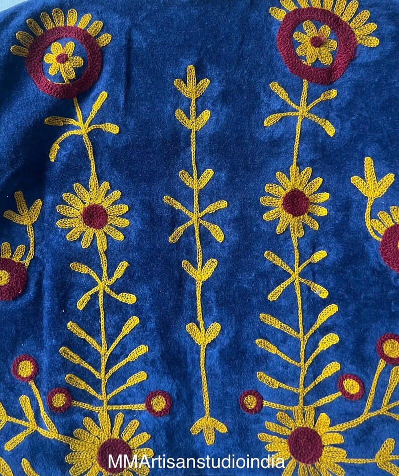 May include: Close-up of a blue textile with embroidered floral patterns in yellow and maroon. The design features stylized sunflowers and other floral elements. The text "MMArtisanstudioindia" is visible at the bottom.