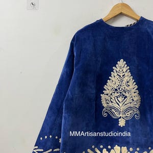 May include: A royal blue velvet jacket featuring intricate cream-colored embroidery. The design includes a large central botanical motif on the back and a decorative border along the hem. The text MMArtisanstudioindia is printed on the fabric.