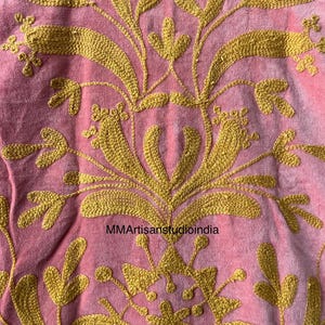 May include: Close-up of a pink textile with intricate gold embroidery. The design features floral and leaf patterns, with the text "MMArtisanstudioindia" visible. The embroidery is detailed and covers most of the fabric.