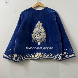 May include: A royal blue velvet jacket featuring cream-colored embroidery. The back displays a large central tree-like motif, with a decorative border along the hem and sleeve cuffs. The text MMArtisanstudioindia is printed in white on the fabric.