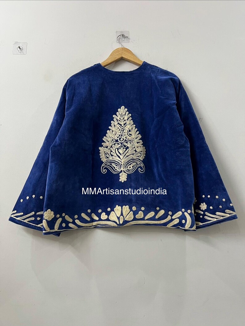 May include: A royal blue velvet jacket featuring cream-colored embroidery. The back displays a large central tree-like motif, with a decorative border along the hem and sleeve cuffs. The text MMArtisanstudioindia is printed in white on the fabric.