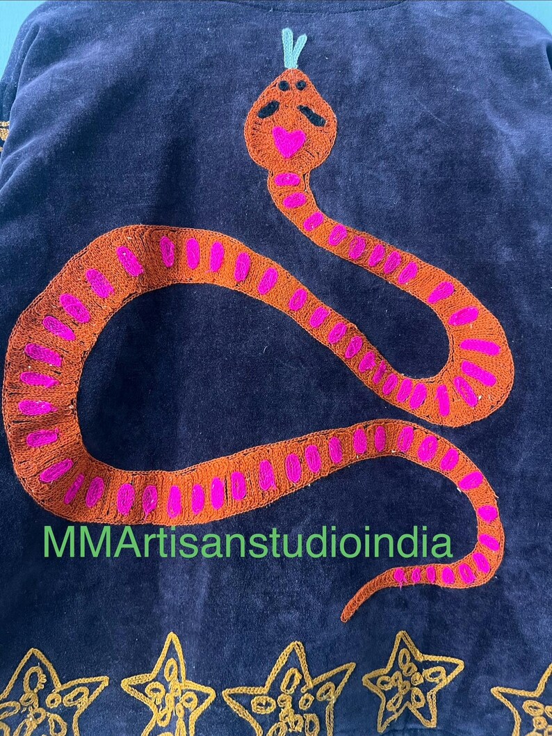 Puede incluir: Tela azul oscuro con un dise&ntilde;o de serpiente naranja bordada con detalles en rosa. La cabeza de la serpiente tiene una boca en forma de coraz&oacute;n. El texto "MMArtisanstudioindia" es visible. Bordado de estrellas doradas en la parte inferior.