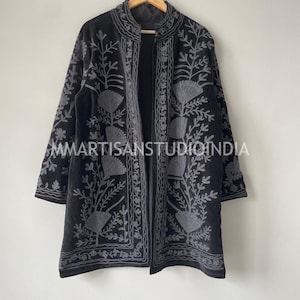 Könnte beinhalten: Eine schwarze, vorne offene Jacke mit aufwendiger grauer Blumenstickerei auf den Vorderteilen und Ärmeln. Das Kleidungsstück hat einen Stehkragen und lange Ärmel, wobei der Text MMARTISANSTUDIOINDIA in der Mitte aufgedruckt ist.