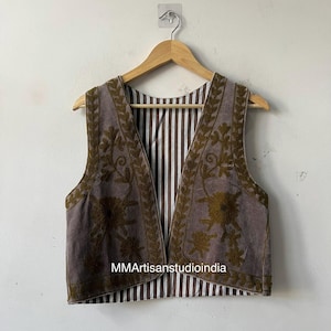 May include: A sleeveless vest with a brown exterior and a striped interior. The vest has embroidered floral designs in a darker brown colour along the edges. The text "MMArtisanstudioindia" is visible on the vest.
