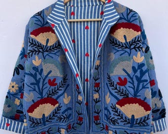 May include: A light blue jacket with floral embroidery in red, beige, and blue. The jacket has a striped lining and cuffs. The embroidery features stylized flowers and leaves, creating a bohemian aesthetic.