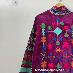 May include: A deep purple velvet jacket with colorful embroidered floral and geometric designs. The jacket features a high collar and long sleeves with detailed embroidery. The text "MMArtisanstudioindia" is visible on the lower right side.