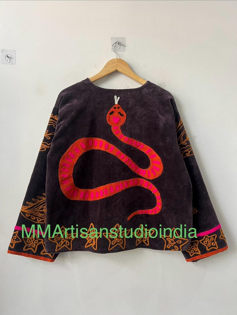 Puede incluir: Top de manga larga marr&oacute;n oscuro con un gran dise&ntilde;o de serpiente bordada en tonos rosa y naranja. Las mangas y el dobladillo presentan bordados decorativos en naranja. El texto "MMArtisanstudioindia" est&aacute; impreso en la parte inferior.
