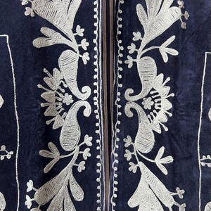 Puede incluir: Primer plano de una chaqueta azul marino con intrincados bordados plateados. El bordado presenta dise&ntilde;os florales y de cachemira, con un borde detallado a lo largo de los bordes. La chaqueta tiene una textura suave y aterciopelada.