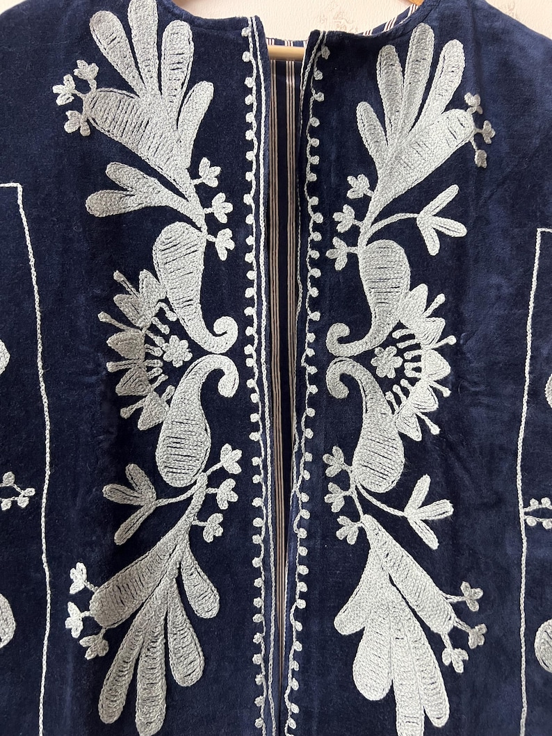Puede incluir: Primer plano de una chaqueta azul marino con intrincados bordados plateados. El bordado presenta dise&ntilde;os florales y de cachemira, con un borde detallado a lo largo de los bordes. La chaqueta tiene una textura suave y aterciopelada.