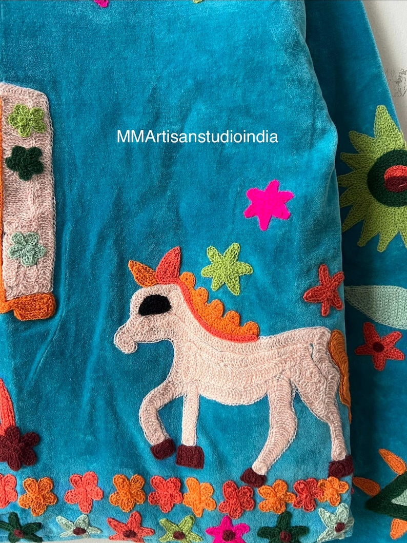 May include: A turquoise textile with embroidered details. A light pink unicorn with an orange mane and tail is featured, surrounded by colorful star and flower accents. The text "MMArtisanstudioindia" is visible.