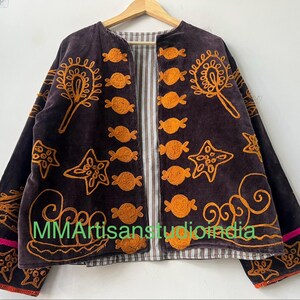 Puede incluir: Chaqueta marr&oacute;n oscuro con dise&ntilde;os bordados en naranja, incluyendo motivos de estrellas y caramelos. La chaqueta tiene un forro a rayas y ribete rosa en las mangas. El texto "MMArtisansstudioindia" es visible.