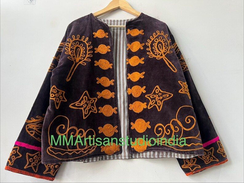 Puede incluir: Chaqueta marr&oacute;n oscuro con dise&ntilde;os bordados en naranja, incluyendo motivos de estrellas y caramelos. La chaqueta tiene un forro a rayas y ribete rosa en las mangas. El texto "MMArtisansstudioindia" es visible.