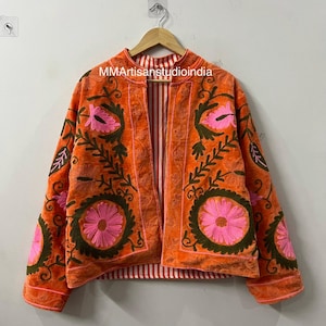 May include: An orange embroidered jacket with pink floral designs and green leaves. The jacket has a striped lining and is hanging on a wooden hanger. The text "MMArtisanstudioindia" is visible on the top.