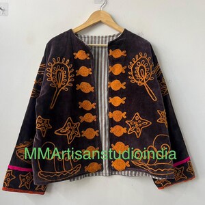 Puede incluir: Chaqueta de terciopelo marr&oacute;n oscuro con bordados naranjas de dise&ntilde;os florales y estrellas. La chaqueta tiene un forro a rayas y ribetes rosas y naranjas. El texto "MMArtisanstudioindia" es visible.