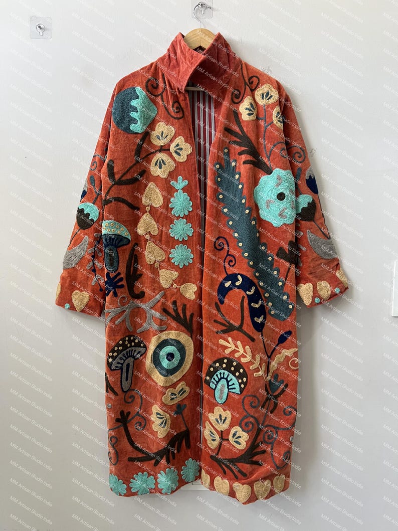 May include: A long, open-front coat in a burnt orange hue, featuring an intricate, multi-colored embroidered pattern of mushrooms, flowers, and abstract botanical shapes in shades of teal, cream, dark blue, and brown, with a striped inner lining.