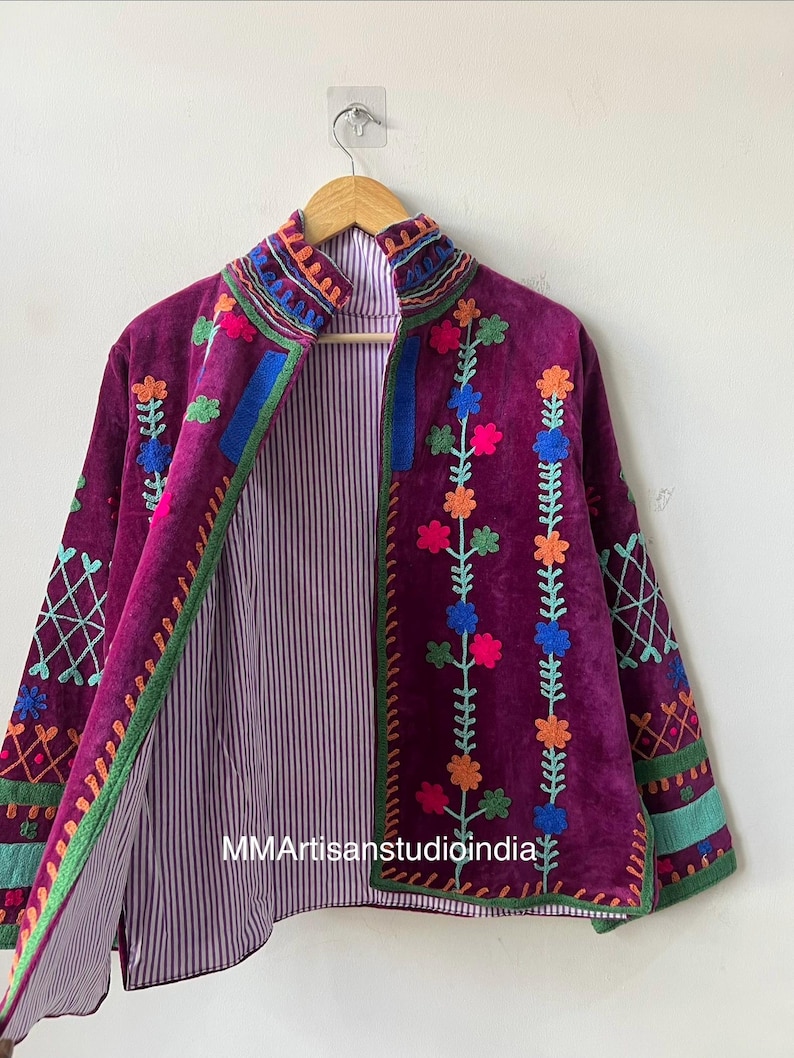 May include: A deep purple embroidered jacket with a high collar, featuring colorful floral and geometric patterns. The jacket has a striped lining and is displayed on a wooden hanger.