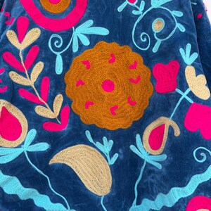 May include: A blue embroidered jacket with vibrant floral and geometric designs. The jacket features a rich navy blue fabric, adorned with bright pink, turquoise, and gold-colored embroidery. The design includes floral patterns, swirls, and heart shapes.