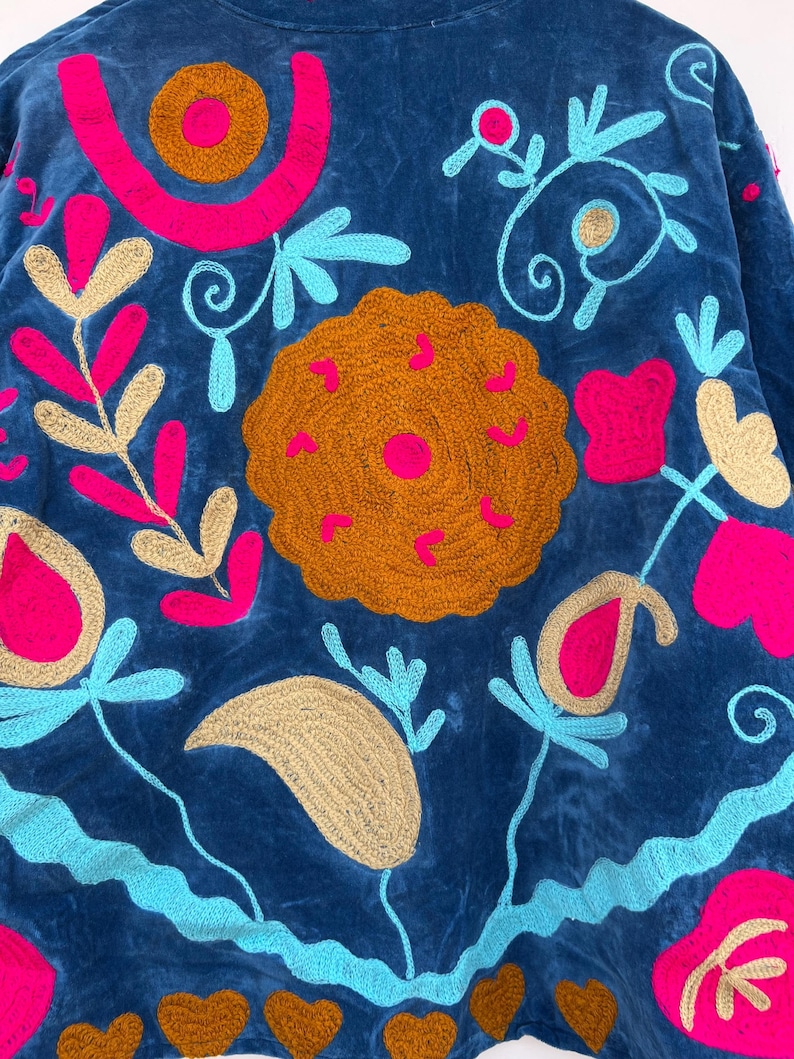 May include: A blue embroidered jacket with vibrant floral and geometric designs. The jacket features a rich navy blue fabric, adorned with bright pink, turquoise, and gold-colored embroidery. The design includes floral patterns, swirls, and heart shapes.