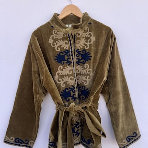 Peut inclure: Veste en velours vert olive avec broderies florales beiges et bleu marine. La veste présente un col mandarin, des manches longues et une ceinture assortie. La broderie est détaillée et couvre le devant et les poignets.