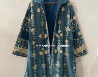 May include: A long, teal-colored velvet coat featuring an open front, a wide collar, and long sleeves. The garment is decorated with vertical rows of gold floral embroidery and geometric patterns. The text MMArtisanstudioindia is visible.