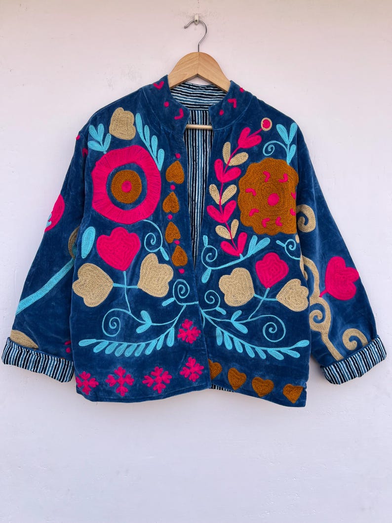 May include: A blue velvet jacket with floral embroidery in pink, gold, and turquoise. The jacket features a striped lining and cuffs. The design includes large flower and leaf patterns.